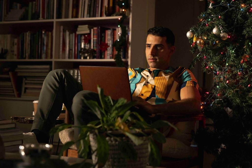 The Holiday Exchange; man sat on a chair against a christmas tree with a laptop