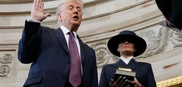 Donald Trump holding his right hand up and his left hand by his side as Melania Trump stands beside him holding two Bibles