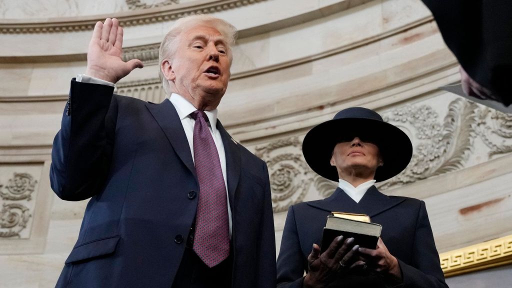 Donald Trump holding his right hand up and his left hand by his side as Melania Trump stands beside him holding two Bibles