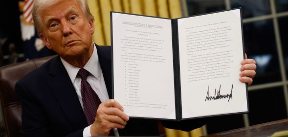Donald Trump holding up a folder containing an executive order.
