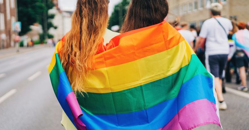 Two people huddled into an LGBT Pride flag.
