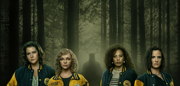 The cast of Yellowjackets in the woodland with a silhouette with horns behind them.