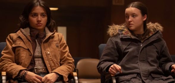 A still from episode one of The Last of Us featuring characters Dina and Ellie sitting on chairs, with Ellie looking over at Dina scornfully.