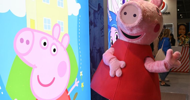 A person dressed as Peppa Pig stands by an illuminated sign