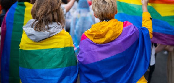 Two young people wrapped in LGBTQ+ flags.