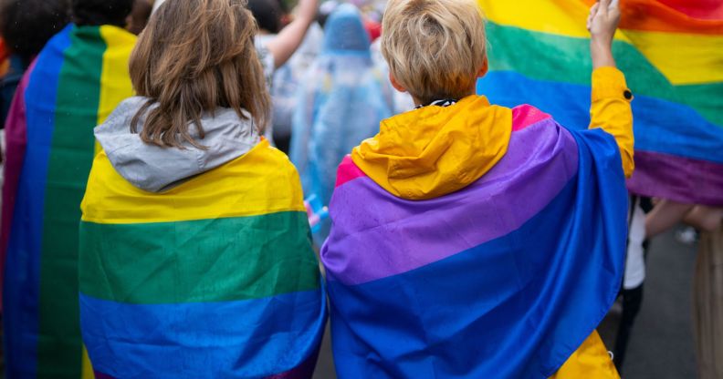Two young people wrapped in LGBTQ+ flags.