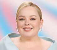 Nicola Coughlan with coiffed blonde hair and a baby blue shoulder piece. She is smiling. Her photo is against a blue pink and white background, reflecting the trans flag colours.