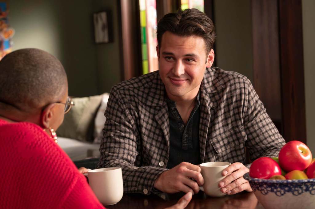 Eddie holding a coffee while talking to Hen at her kitchen table. 