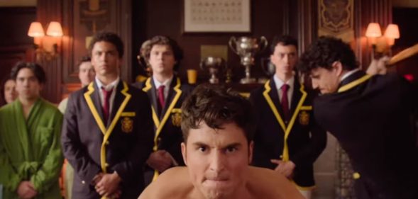 A still from Overcompensating featuring Benito Skinner on all fours in skimpy underwear preparing to be hit on the backside by a cricket bat held by Adam DiMarco.