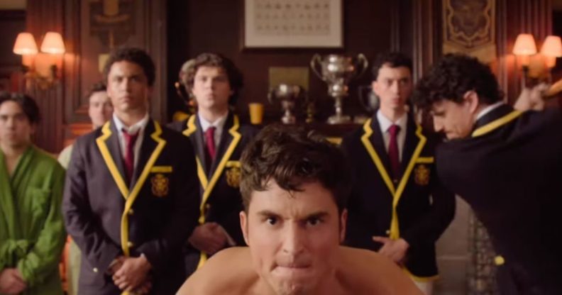 A still from Overcompensating featuring Benito Skinner on all fours in skimpy underwear preparing to be hit on the backside by a cricket bat held by Adam DiMarco.