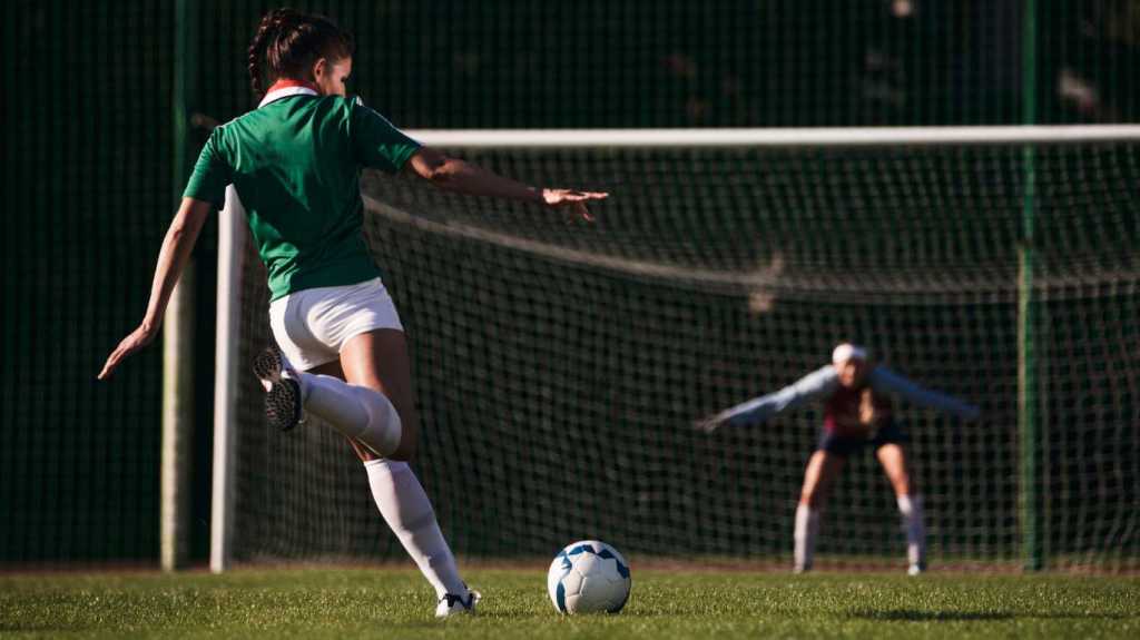 Two female soccer players with soccer ball playing on soccer field. Penalty shot.