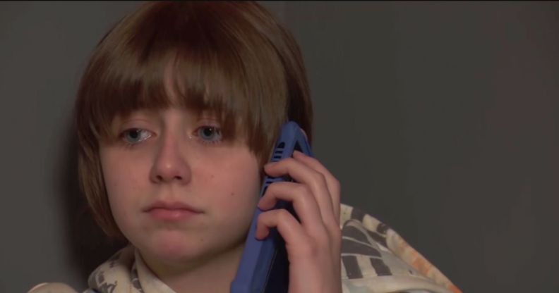 Ava Webster as Ro Hutchinson in looks teary as they hold a blue phone in upcoming scenes from soap Hollyoaks.