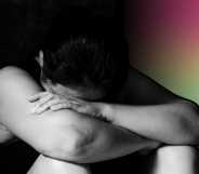 A person in black and white sits with their head in their arms in front of a rainbow hue