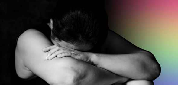 A person in black and white sits with their head in their arms in front of a rainbow hue