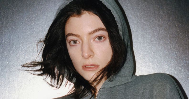 Lorde in a grey hoodie with brown hair poking out while standing against a grey background as she released 'Virgin'