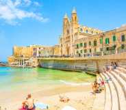 Balluta Bay beach in St Julian's town, Malta travel photo with young people chilling on the beach.