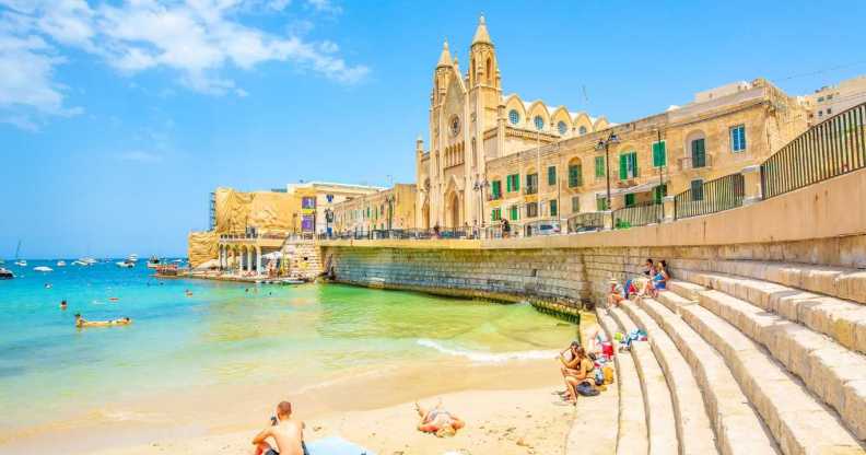 Balluta Bay beach in St Julian's town, Malta travel photo with young people chilling on the beach.
