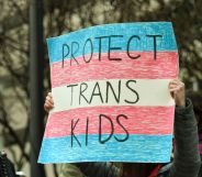 A person holds up a sign reading 'protect trans kids'.