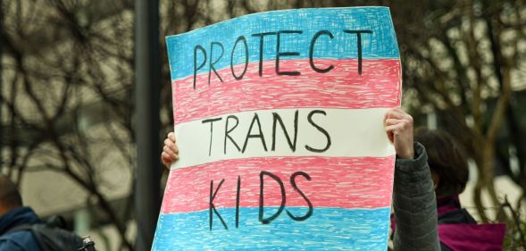 A person holds up a sign reading 'protect trans kids'.