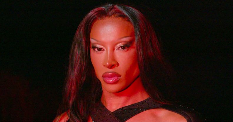 Drag star Tayce in full drag standing in a dark room with a red light shining on her face.