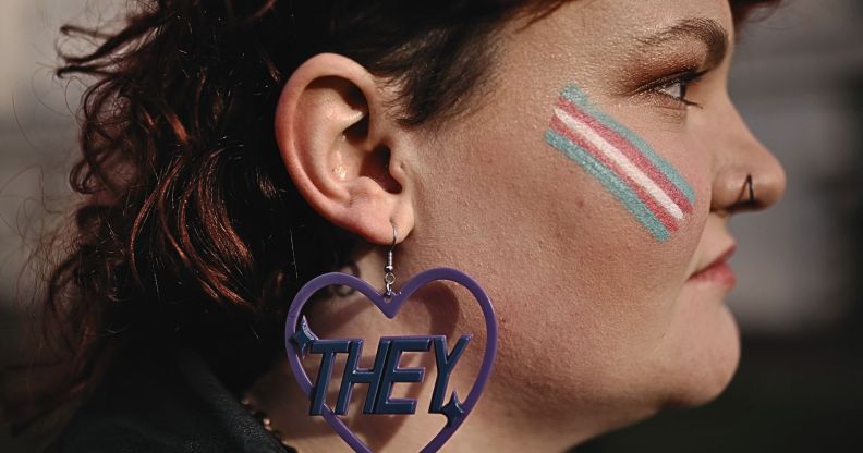 The side-profile of a trans person wearing earrings that read "they".