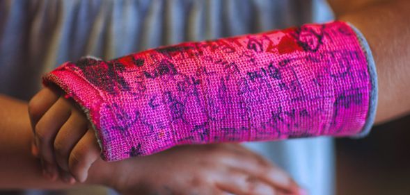 A young person with a pink cast for a broken wrist that has been drawn on.