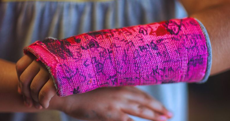 A young person with a pink cast for a broken wrist that has been drawn on.