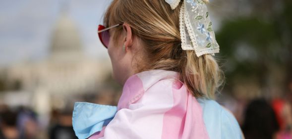 The back of a person wearing a trans flag as a cape.