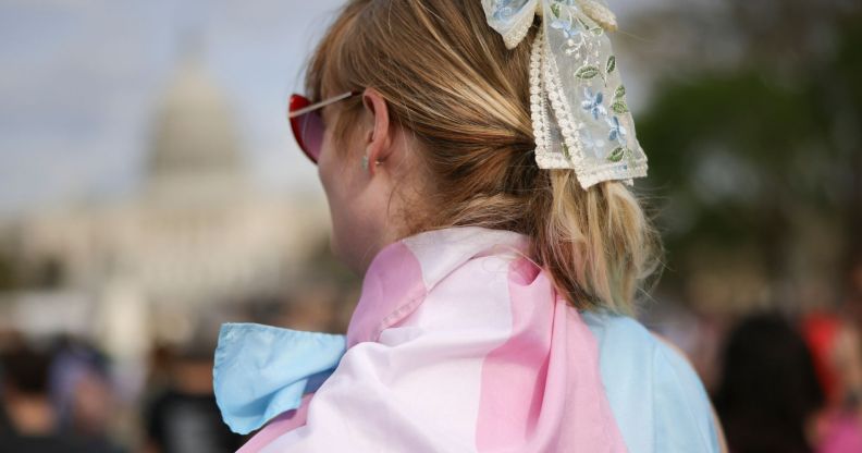 The back of a person wearing a trans flag as a cape.