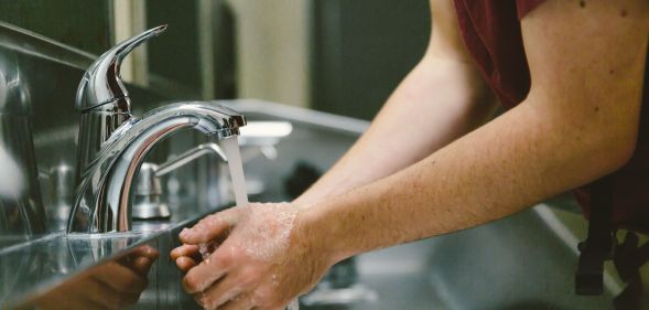 A person washing their hands in a public toilet.