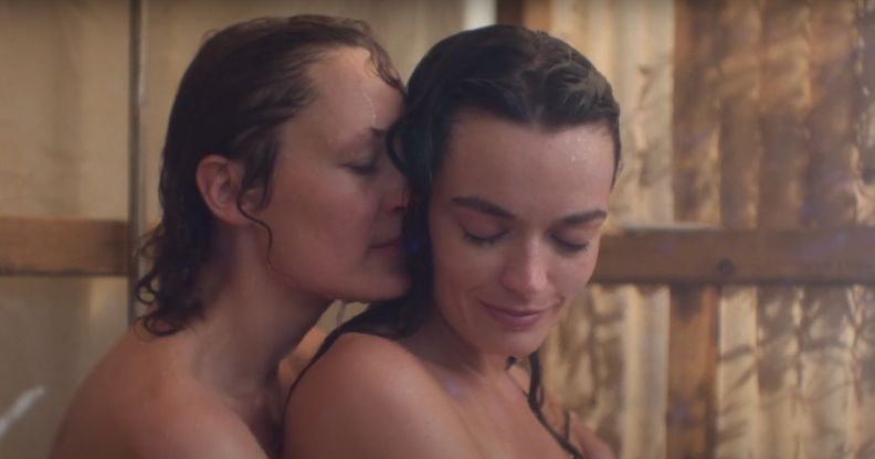 A still from the trailer of new film hot milk showing a nude Vicky Krieps and Emma Mackey embracing in a shower while smiling.