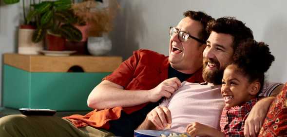 Fathers with adopted daughter laughing together on sofa.