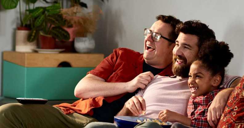 Fathers with adopted daughter laughing together on sofa.