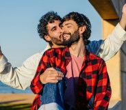 Mid-adult male gay couple embracing while holding LGBTQ+ flags outdoors in Barcelona in Spain.