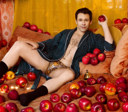 Bryan Safi wearing leopard print underpants and an open robe. He is laying on a sofa covered in apples.