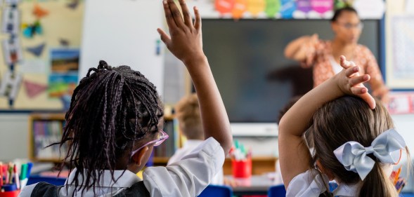 Primary school students sitting in a classroom being taught by a teacher.