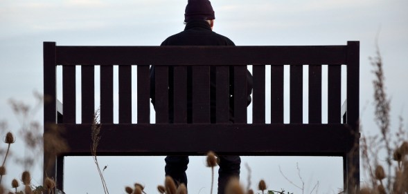 A man sits alone on a park bench.