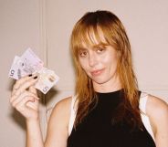 Gordi in a black vest top holding up notes of cash and smiling.