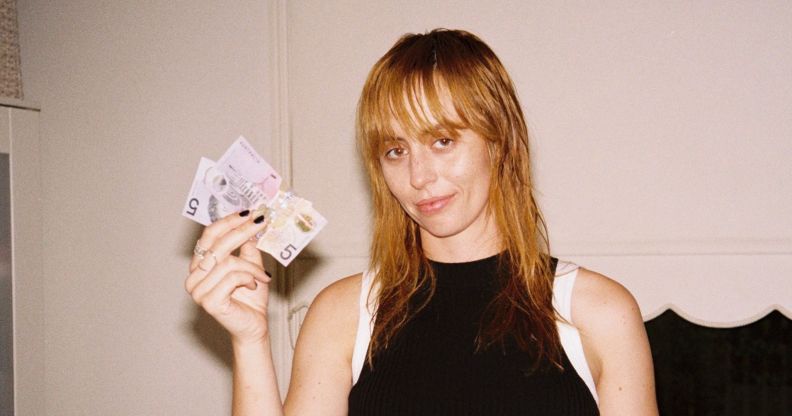 Gordi in a black vest top holding up notes of cash and smiling.