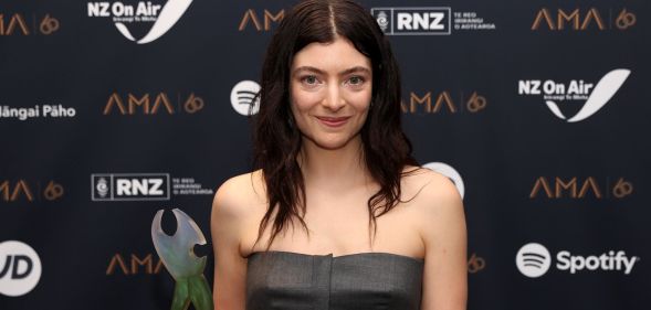 Lorde smiles on a red carpet wearing a grey sleeveless top.