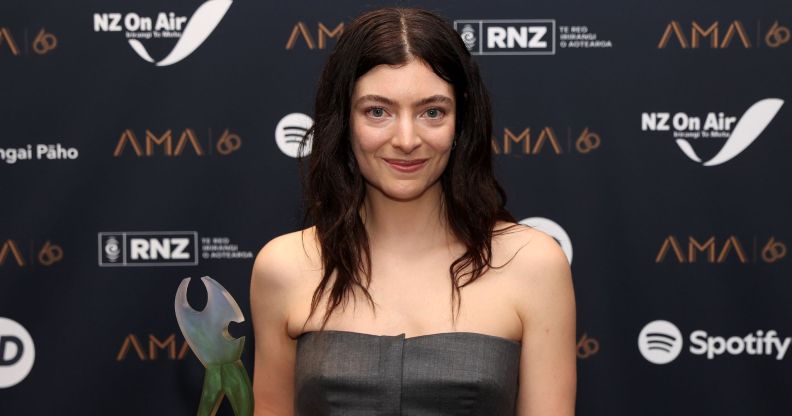 Lorde smiles on a red carpet wearing a grey sleeveless top.