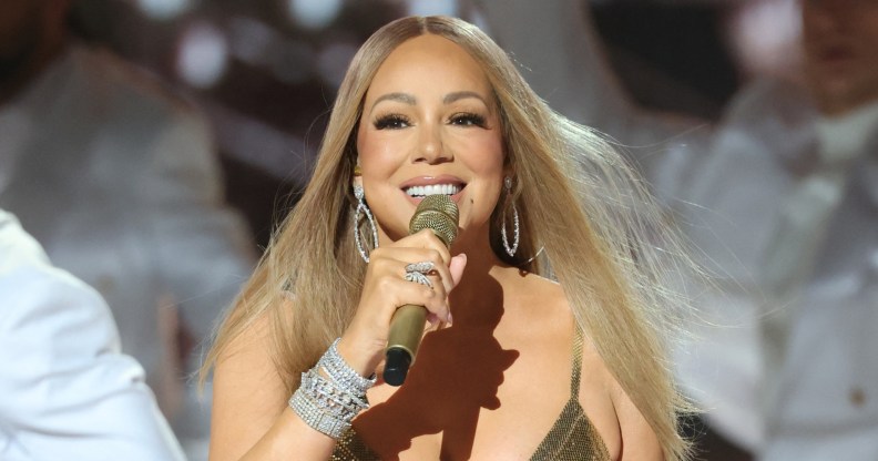 Mariah Carey performing while wearing a gold dress, singing into a gold mic.