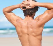 A naked man flexing on a beach.