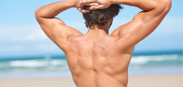 A naked man flexing on a beach.