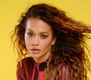 Rita Ora in a black and red top posing against a yellow and red background.