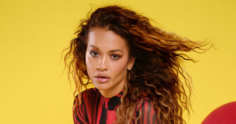 Rita Ora in a black and red top posing against a yellow and red background.
