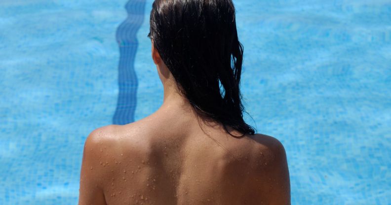 The back of a topless woman looking over a pool.