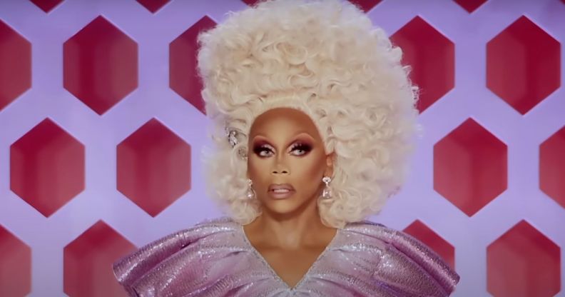 RuPaul watching a lip-sync in episode one of RuPaul's Drag Race season 13, wearing a nimbus cloud of blonde hair and a glittering purple dress