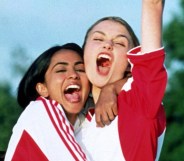 Jess (Parminder Nagra) and Jules (Keira Knightley) in red and white football kits hugging eachother and yelling in celebration.