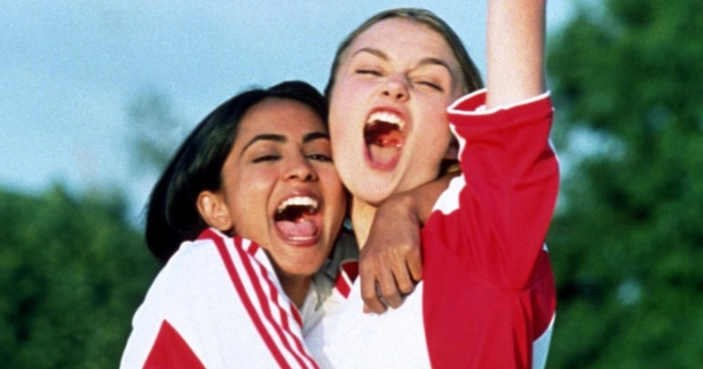 Jess (Parminder Nagra) and Jules (Keira Knightley) in red and white football kits hugging eachother and yelling in celebration.